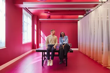 Two people sitting on a ping pong table in a brightly colored room