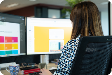 Persona trabajando en un escritorio con dos monitores que muestran contenido colorido