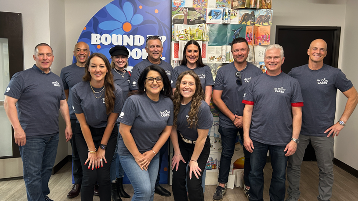 Group photo of ten people wearing matching gray shirts, posing together in an office setting